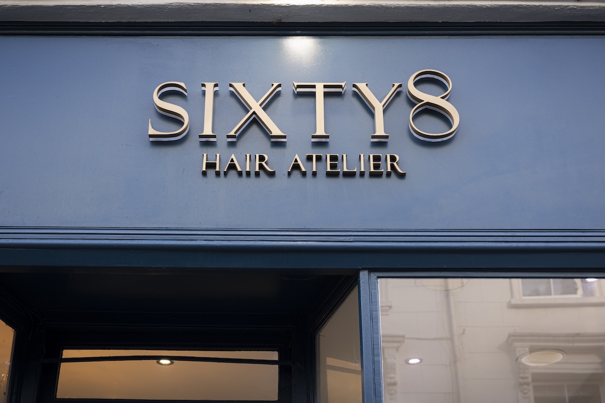 A blue shopfront sign with metallic letters reads SIXTY8 HAIR ATELIER, reflecting the nearby lights and buildings—right in the heart of Maida Vale’s Hottest Dining Destinations.